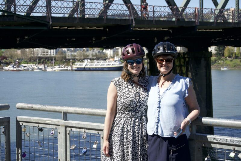 Two women cyclists standing together and smiling at the portland waterfront